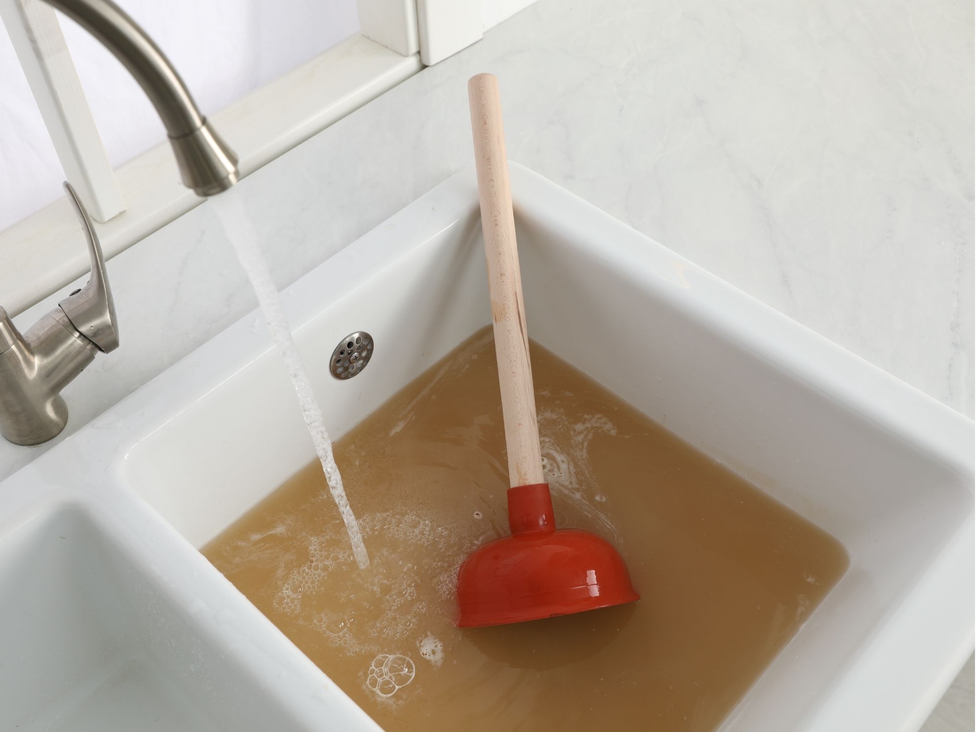 Clogged sink with dirty standing water and a plunger